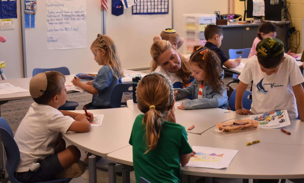 Hillel Torah kindergarten teacher supporting a kindergarten student at her desk, highlighting personalized Jewish day school education in Chicago.