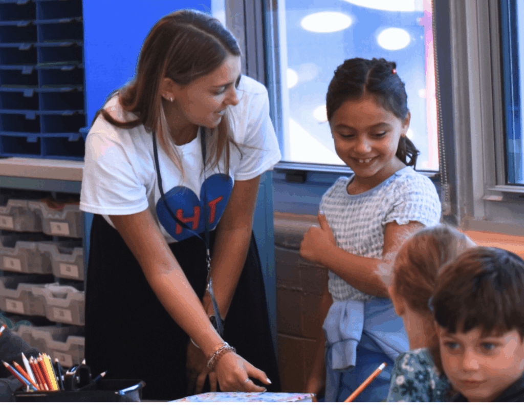 Hillel Torah second grade teacher connecting warmly with students in an engaging classroom environment.
